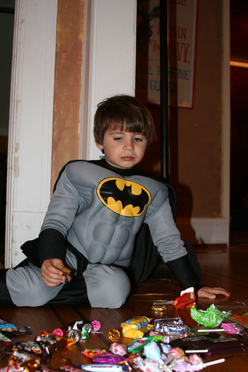 a little boy in his batman costume sitting on the ground