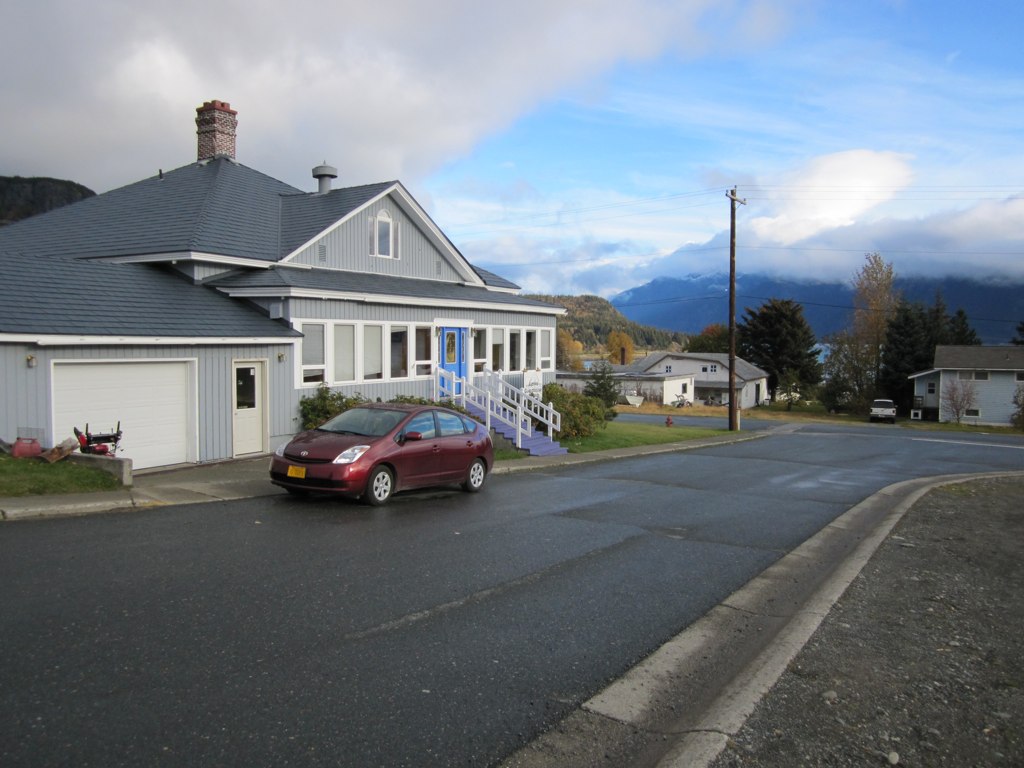 a red car sits in front of a gray house