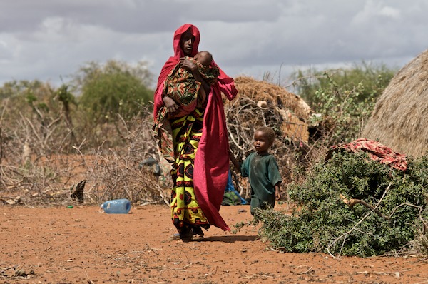 a woman carrying a child walks through the barren area