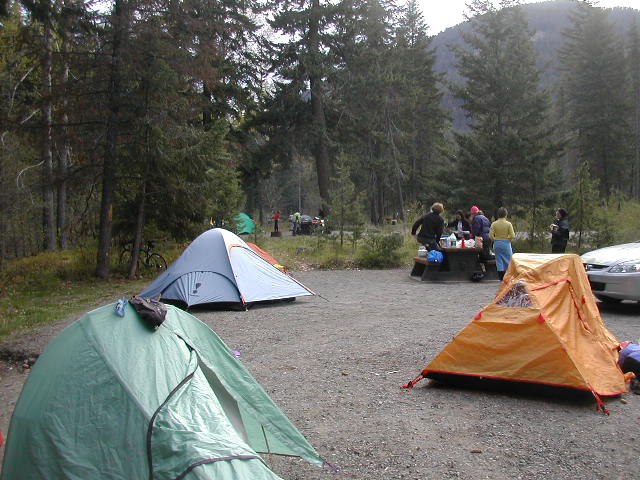 a tent, car, and several people at a campsite with trees