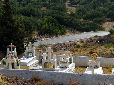 some graves in a field by trees and a road