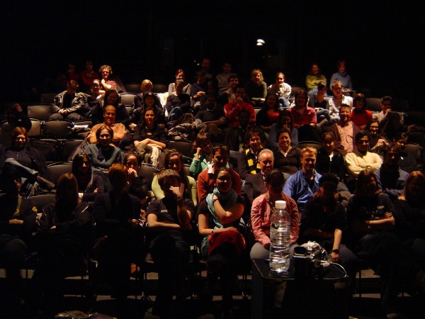 a crowd of people sitting in a theater filled with empty seats