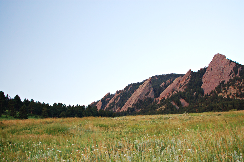 a beautiful mountain range in the grass with a blue sky