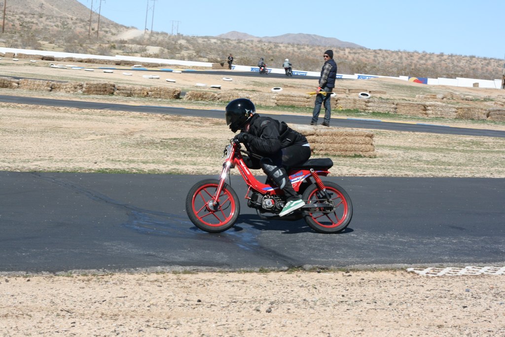 a person rides a motorcycle while another man looks on