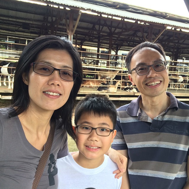 the couple poses for a picture with their son in front of the animal enclosure