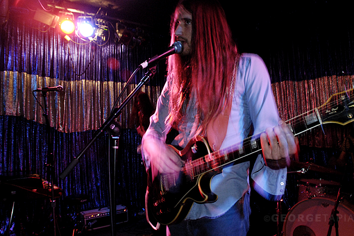 long - haired man with guitar plays on stage