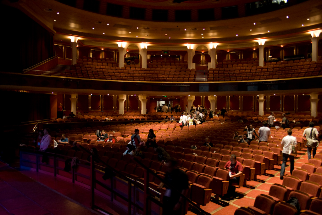 a theater auditorium with many seats and people milling around