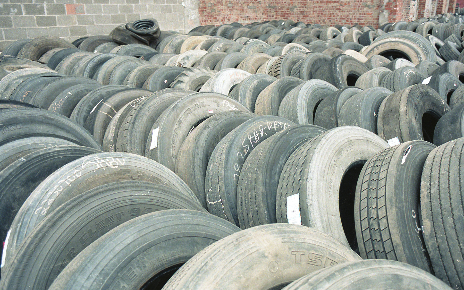 rows and piles of used, old tires sitting against a brick wall