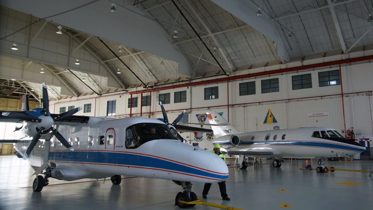 two airplanes in hanger with men standing next to one plane