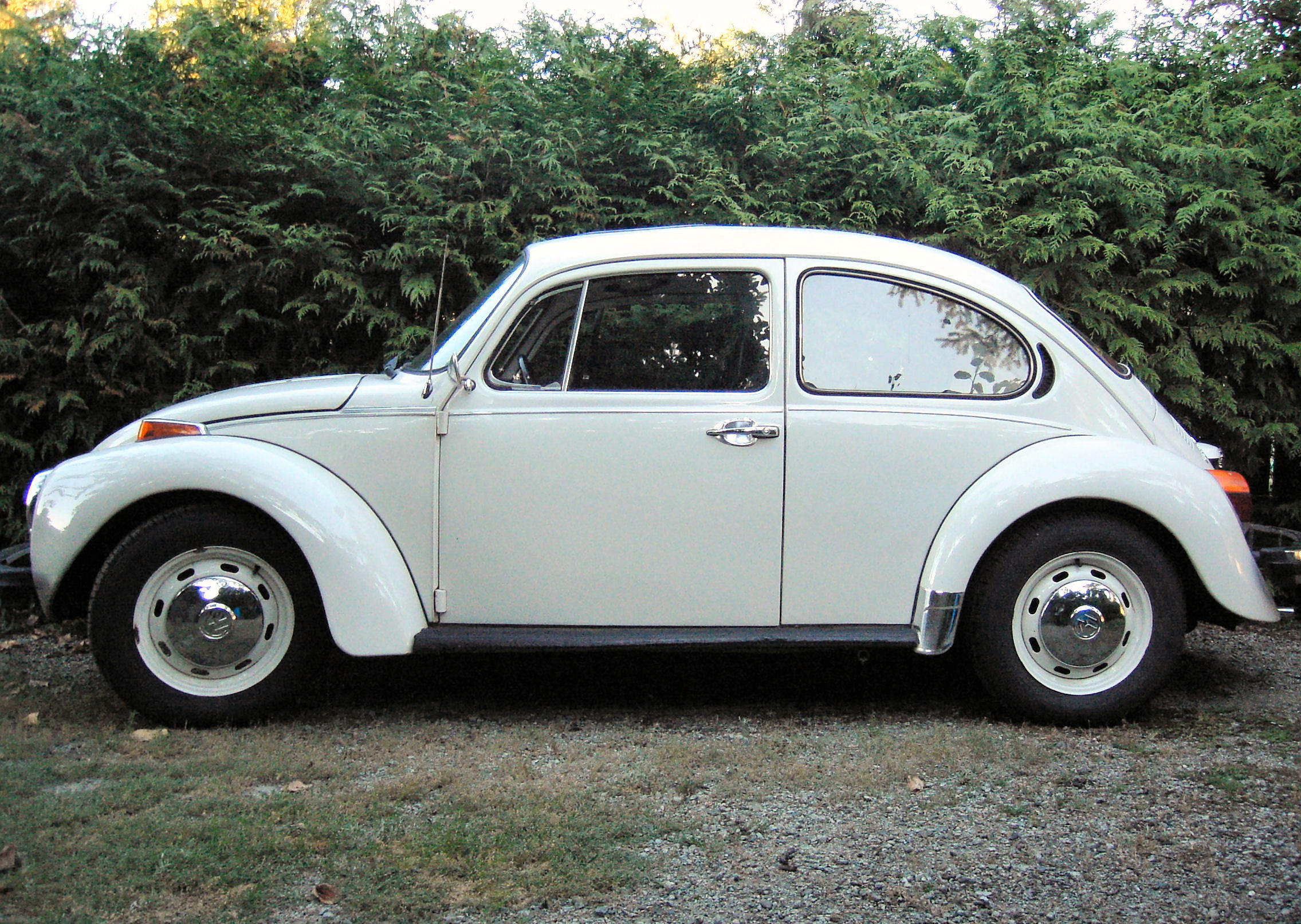 an old white vw bug is parked in a gravel area
