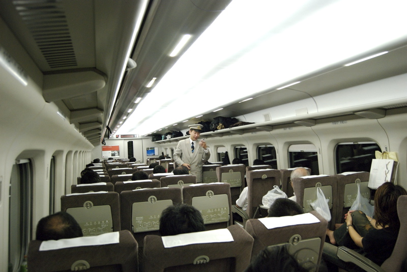 a passenger train car with lots of empty seats and people sitting down
