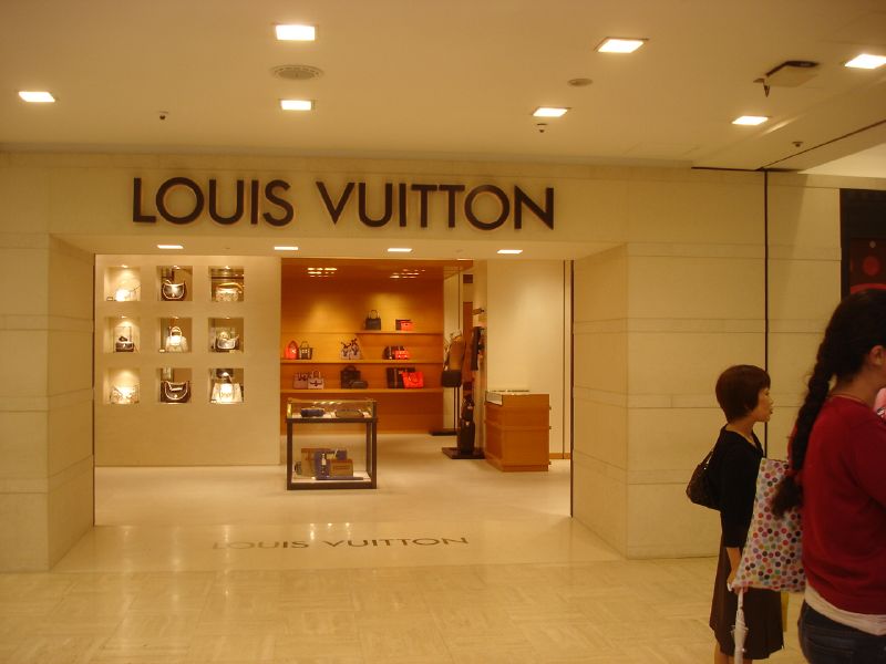 two people in front of a store with a sign for louis vuitton