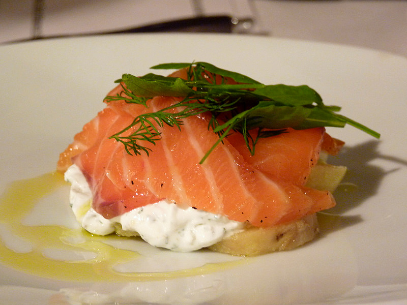 a piece of fish on a white plate topped with whipped cream and dilling