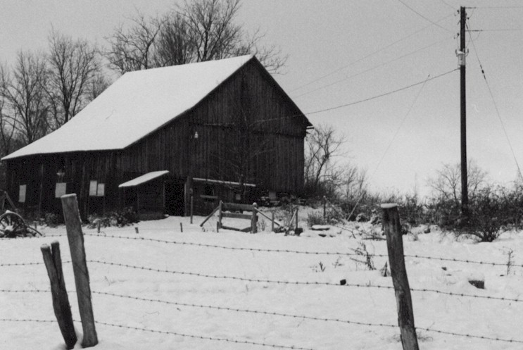 an old barn sits near some tall grass and trees