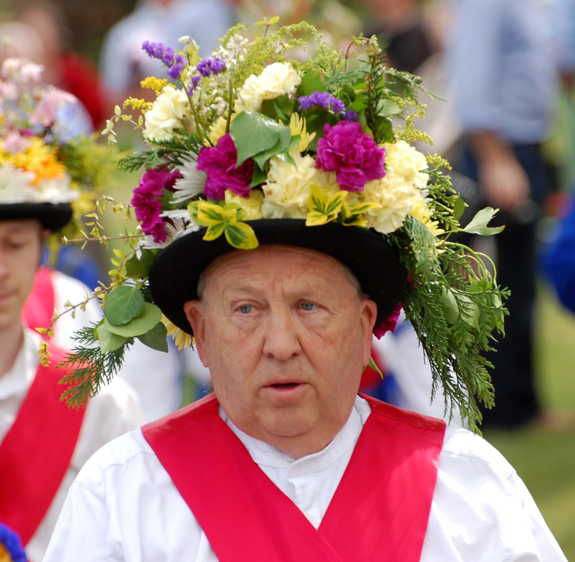 a man in a flowered hat stands between other men in traditional clothing