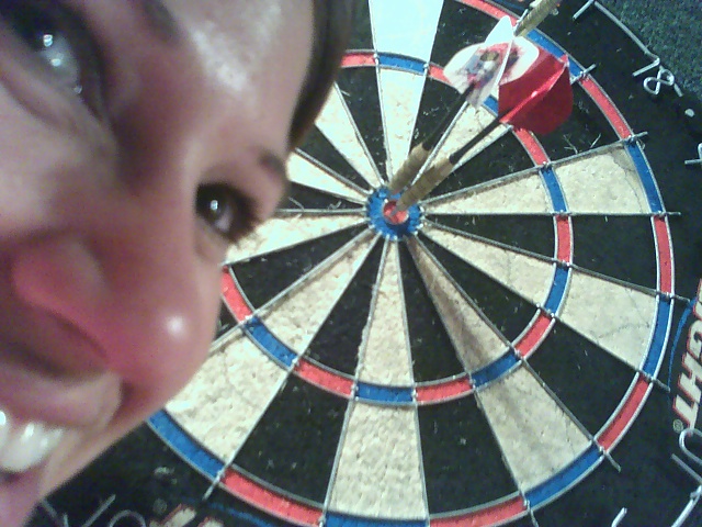 a young woman is smiling for the camera and she has a toothbrush on her mouth near a dart board