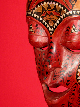 a wood mask is standing against a red wall