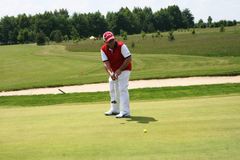a man in a red and white outfit holds a golf club as he stands by the green