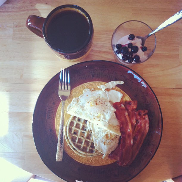 some bacon and eggs on a plate by a mug of coffee