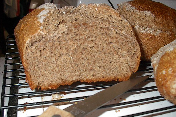two loaves of bread sitting on a cooling rack next to a knife