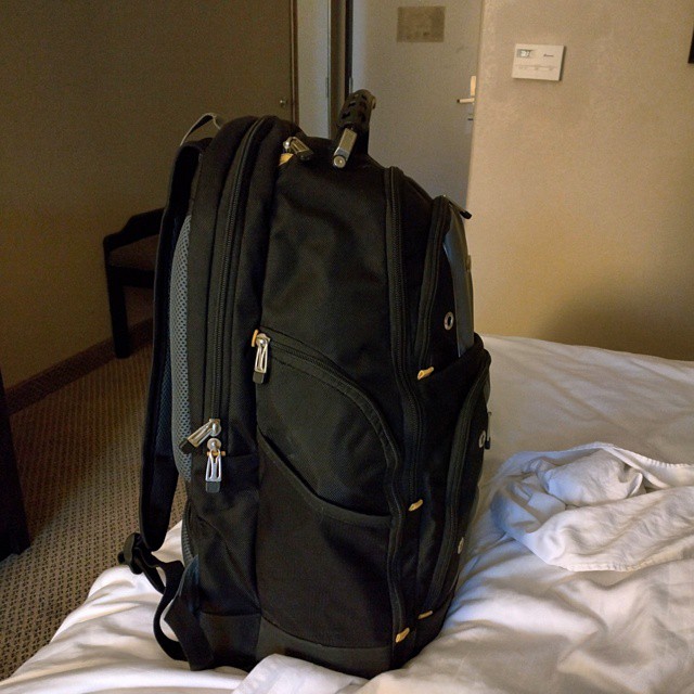 a backpack is sitting on the bed while someone sits on the pillow