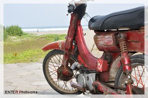 an old red moped parked next to a sandy beach
