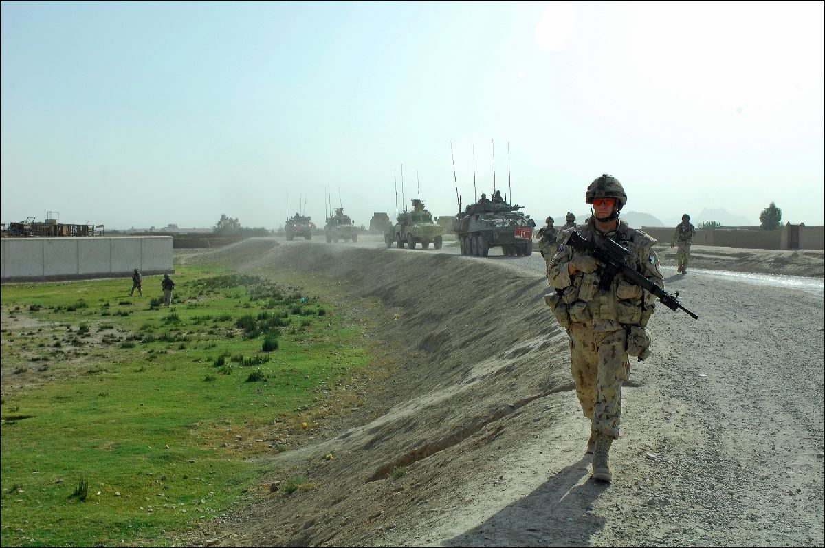 the soldiers are walking on the road with their armored vehicles