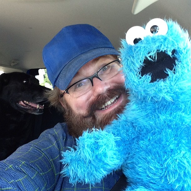 a bearded man is holding a blue furry sesame street monster