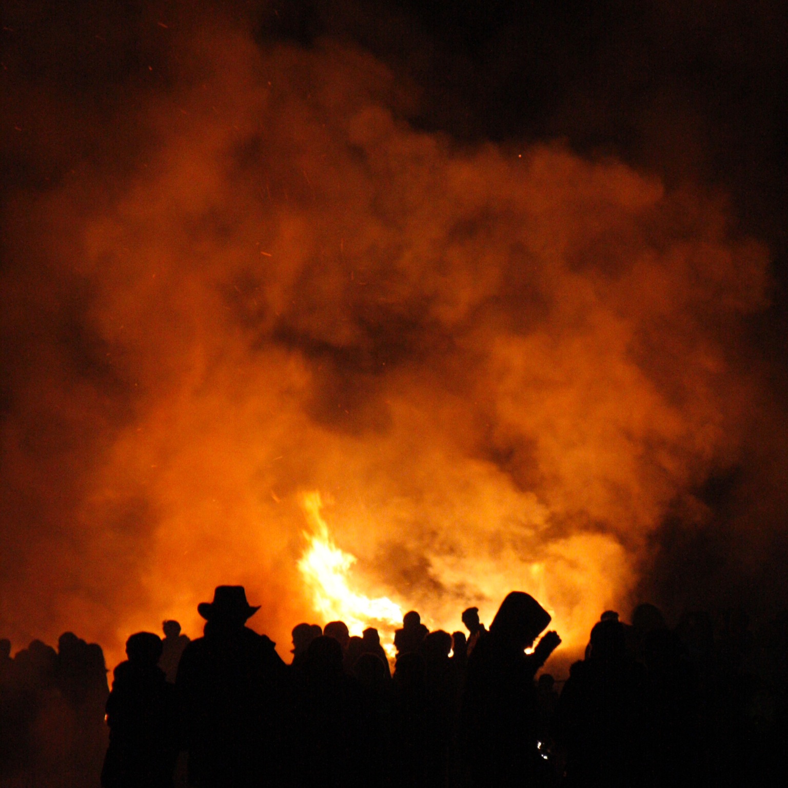 a crowd of people standing around a huge orange fire