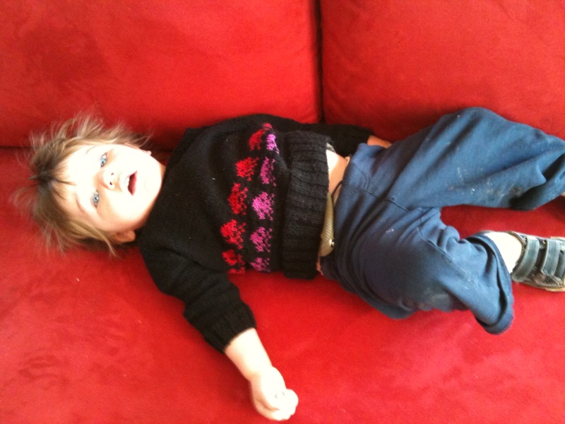 child laying on red couch with one foot up