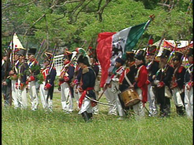 a line of people marching in uniforms with a large flag