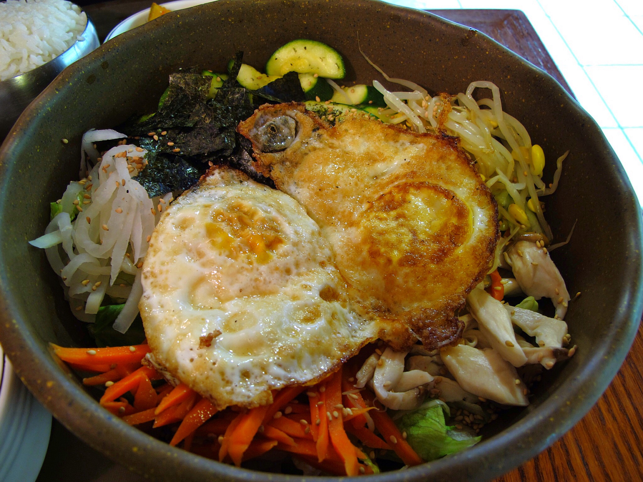 an oriental dish in a bowl with a fried egg, carrots, noodles and broccoli