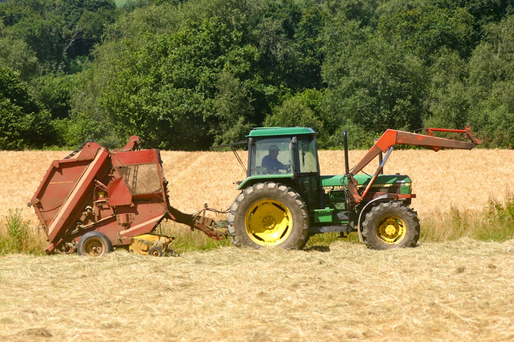 a green tractor is driving in a wheat field