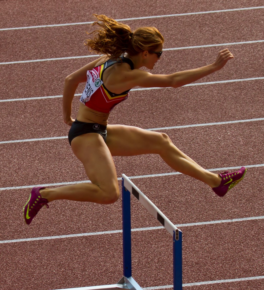 a woman jumping over a hurdle onto a metal rail