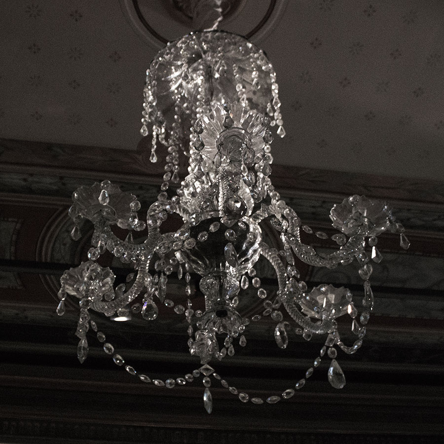 a chandelier hangs in a dark room with mold work on the ceiling