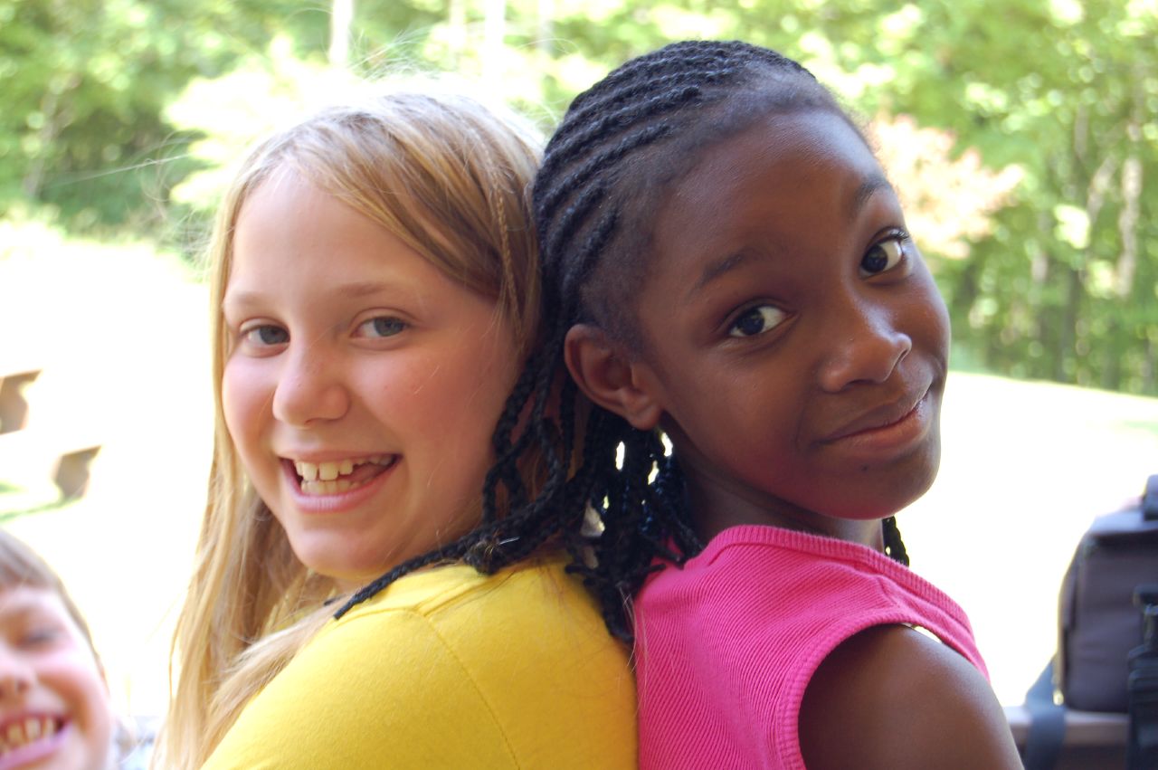 two girls are smiling for the camera and some trees