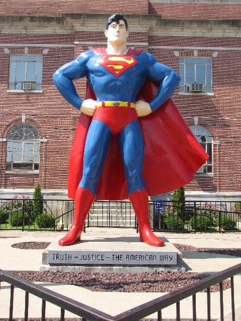 a statue of superman stands on a bench in front of a brick building
