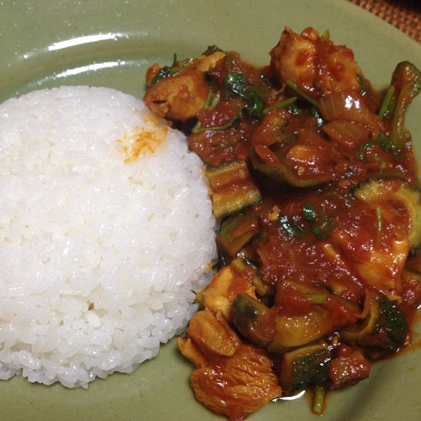 a green plate holding rice, veggies and sauce