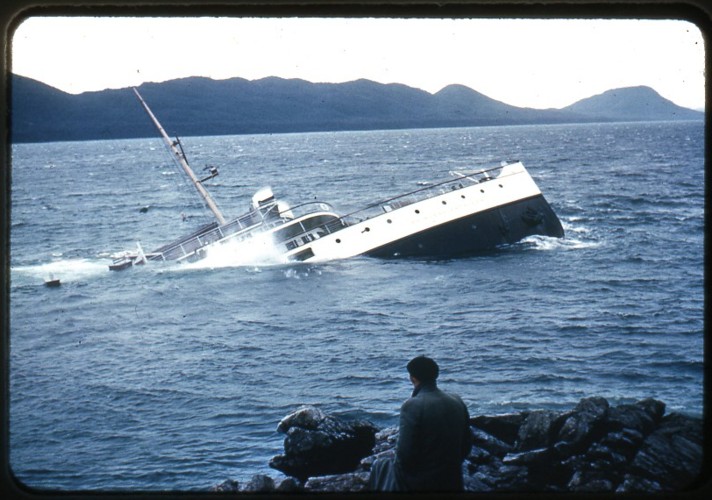 an old picture of a man standing next to a ship in the ocean