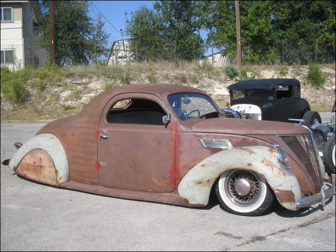 a rusty old car sits on the street