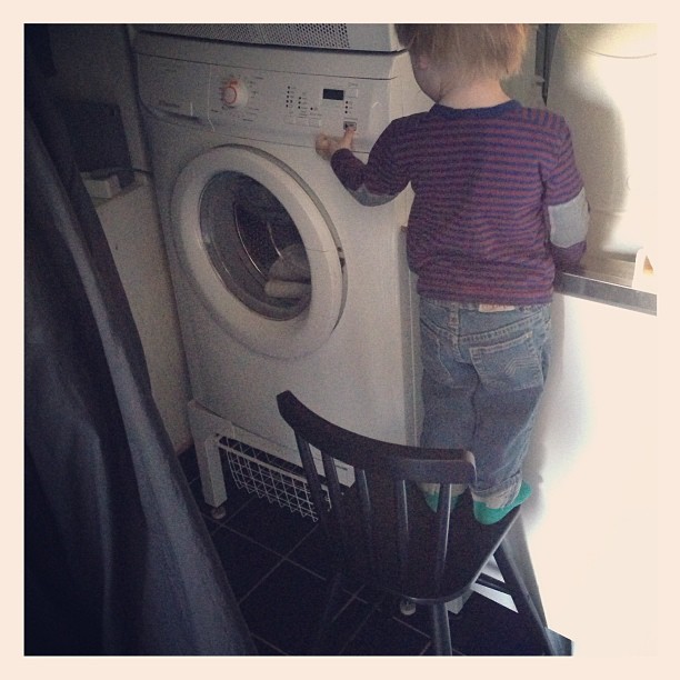 a toddler standing on a washer next to a washing machine