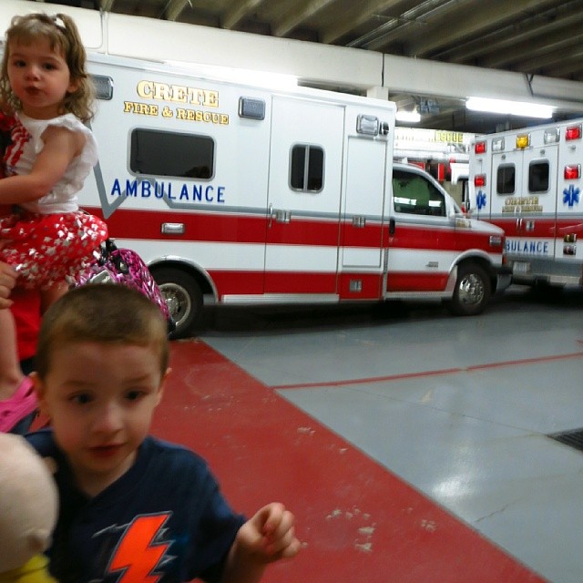 two children sit on a bench with an ambulance in the background