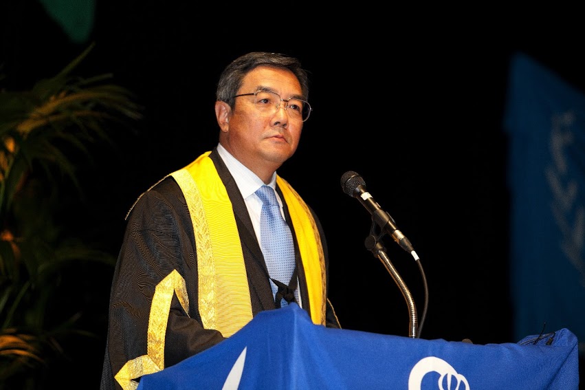 a man is standing in front of a microphone in a graduation gown