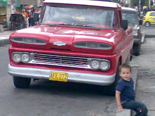 a little boy sits on the edge of a curb and looks up at an old red truck
