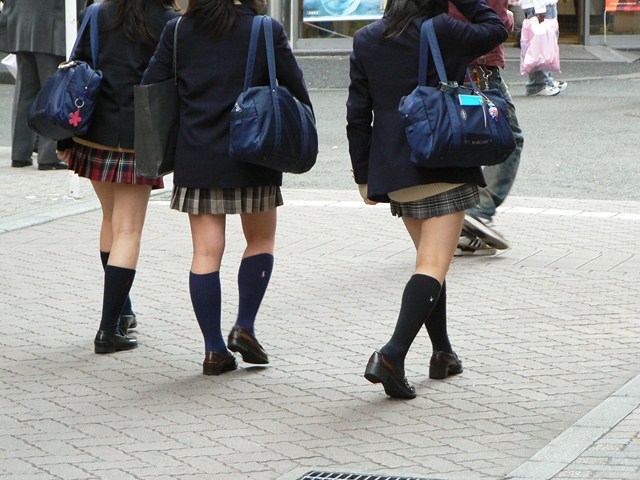 three girls are walking down the street holding backpacks