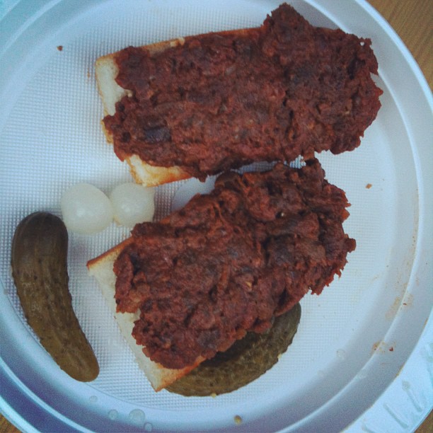 a white paper plate with pickles and two meat sandwiches