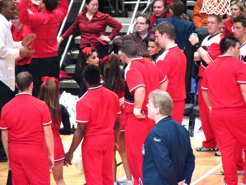 a group of people wearing red shirts and some standing around a basketball court