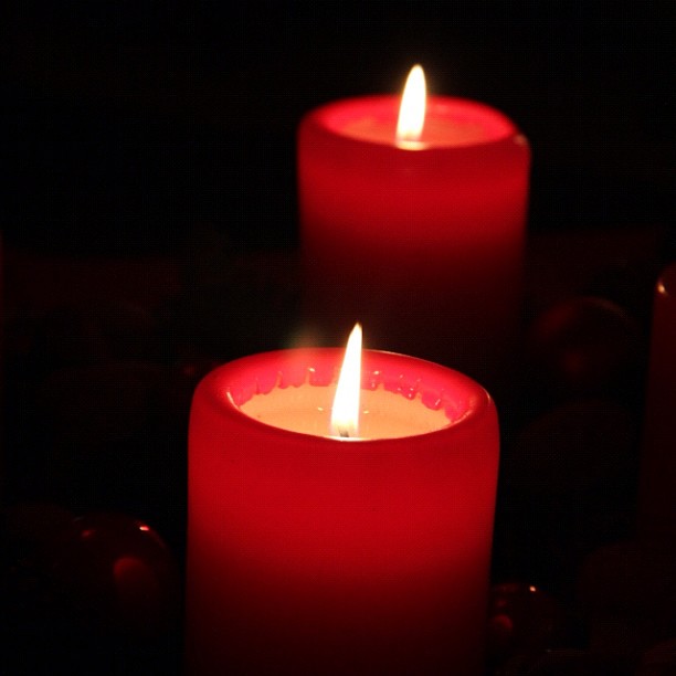 four candles lit in the dark with one burning