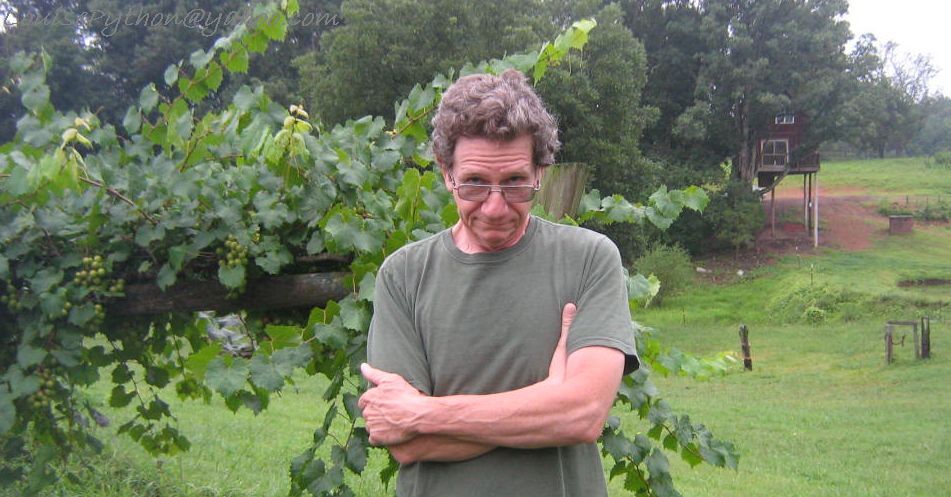 a man in glasses standing by a tree