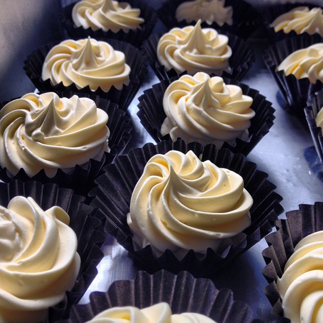 many cupcakes with yellow frosting on them are arranged in a display case